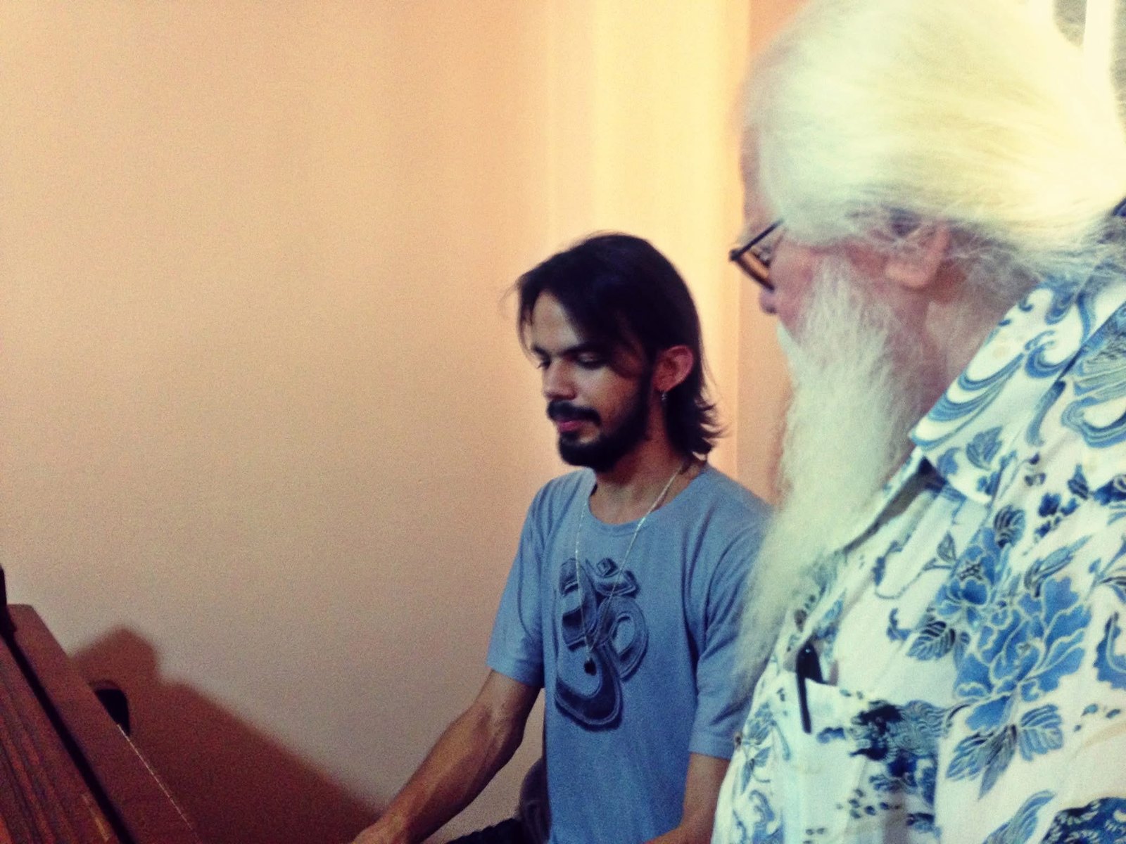 Salomão Soares, jovem, ao piano, com Hermeto Pascoal de pé ao seu lado, ouvindo