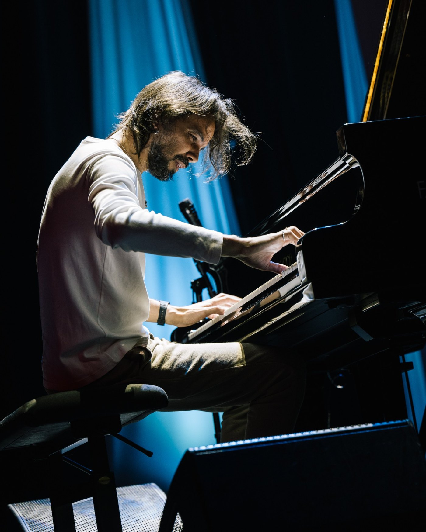 Salomão Soares ao piano de cauda no Cape Town International Jazz Festival, debruçado sobre o teclado, sob luz azul de palco